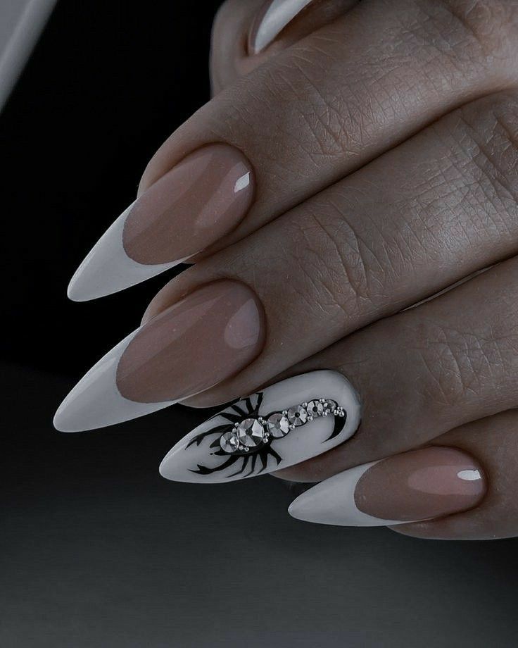 Pointed almond-shaped fingernails with white tips and a scorpion design on one nail with rhinestones.