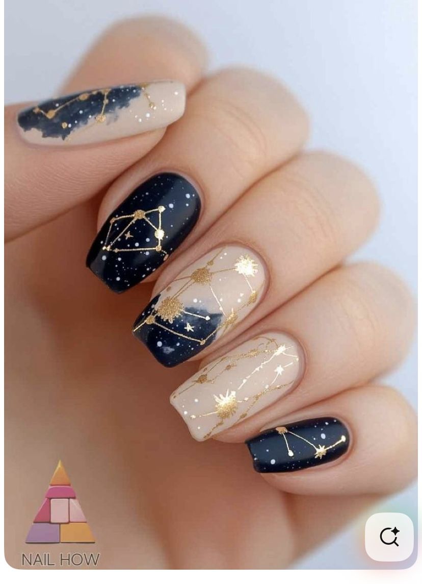 Close-up of a hand with celestial-themed nail art. Alternating nails feature a dark navy base with white speckles and gold…