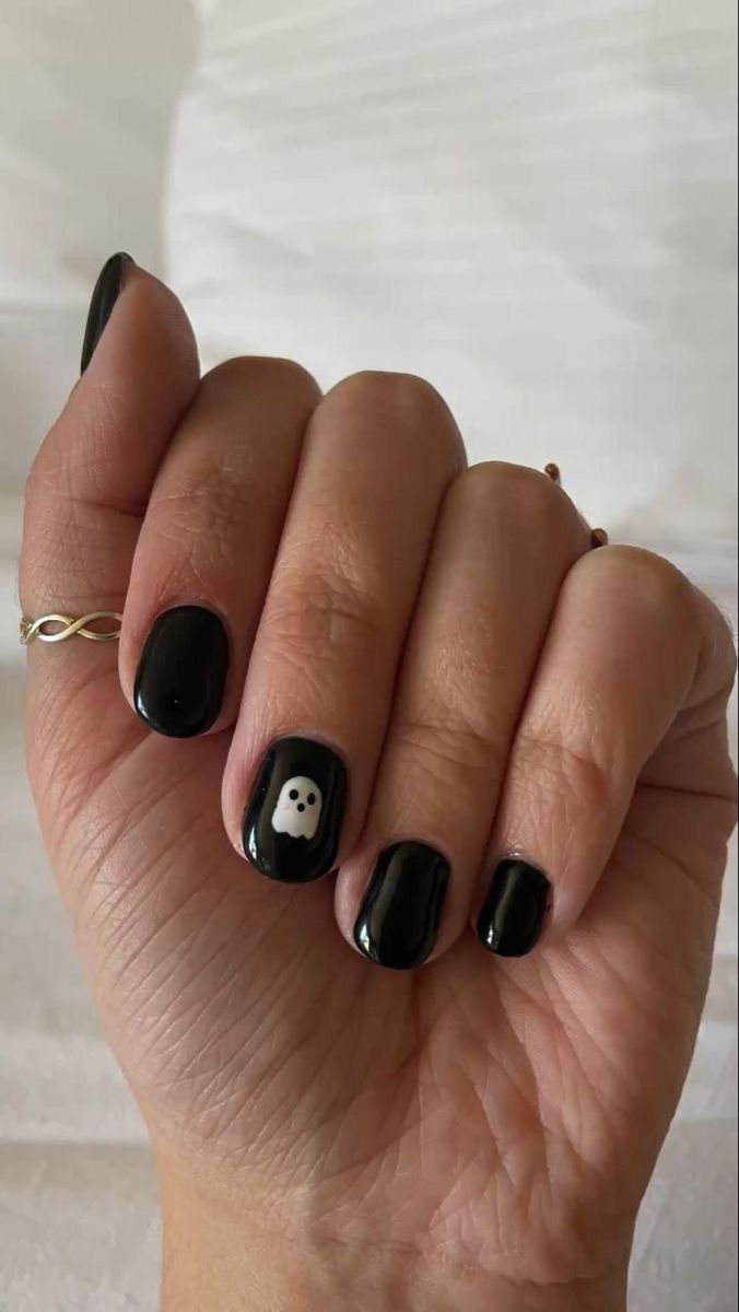 Hand with short black nails, one nail features a small white ghost design.