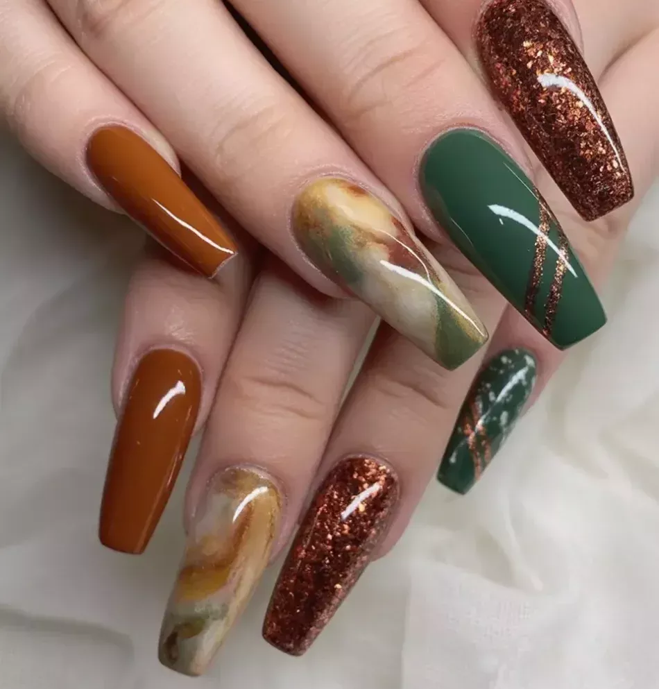 Close-up of coffin-shaped nails featuring solid brown-orange, marbled earth tones, rich forest green, and shimmering copper…
