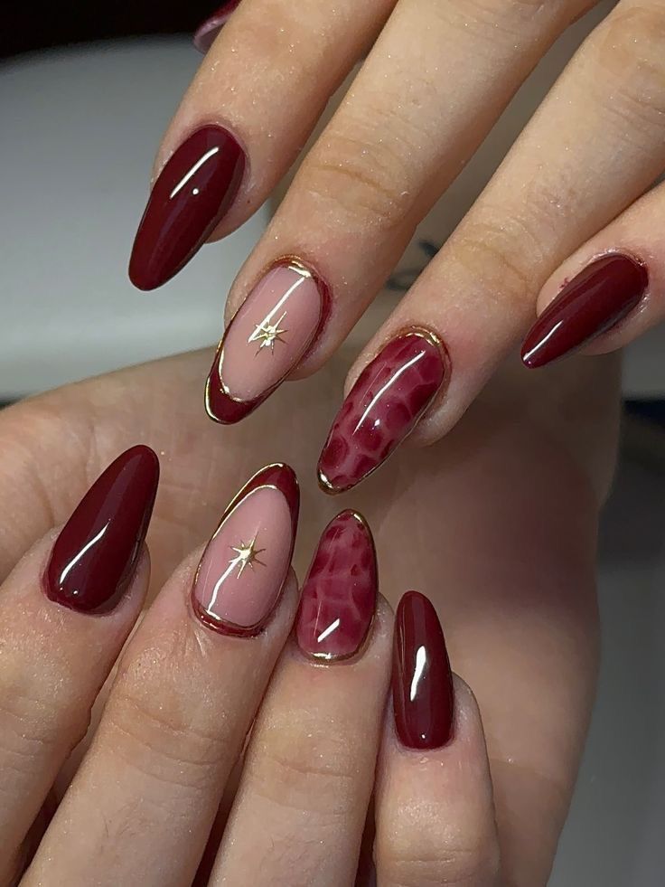 Close-up of manicured hands with dark red, blush pink outlined in gold, and textured red nails.