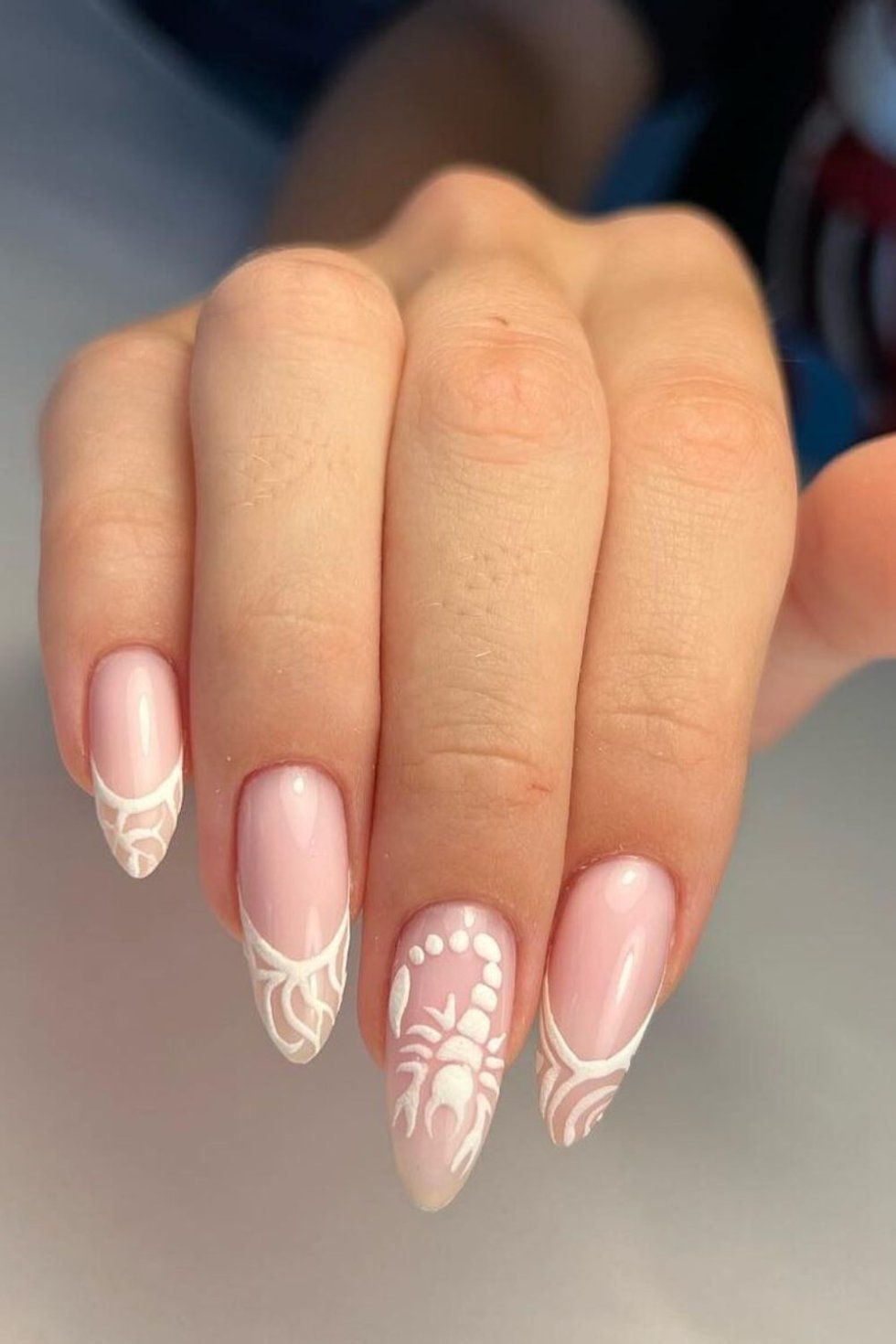 Almond-shaped nails with a clear base and white designs. One nail features a scorpion, while others have abstract art on the…