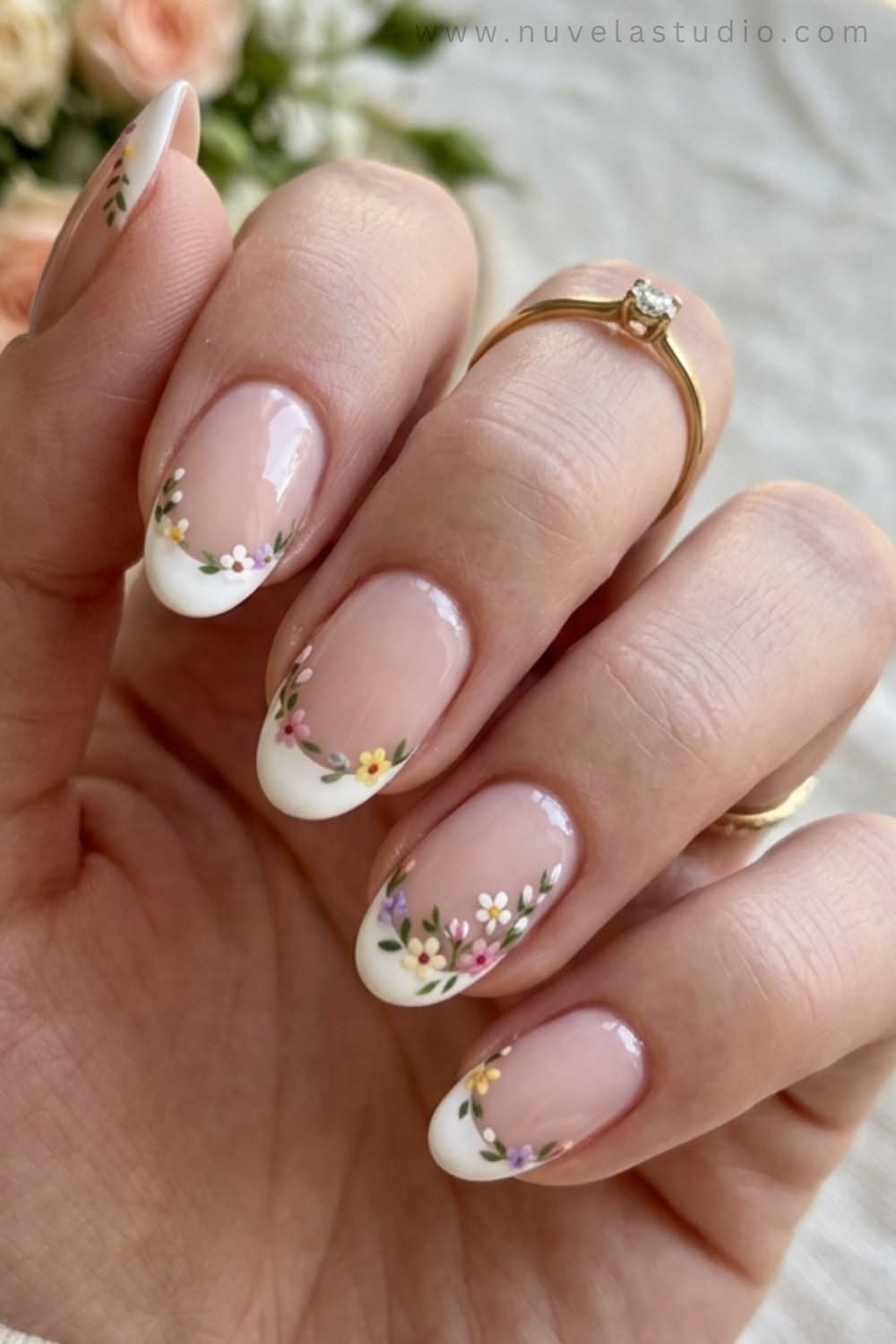 Close-up of a hand with manicured nails, featuring white French tips adorned with tiny colorful painted flowers along the…