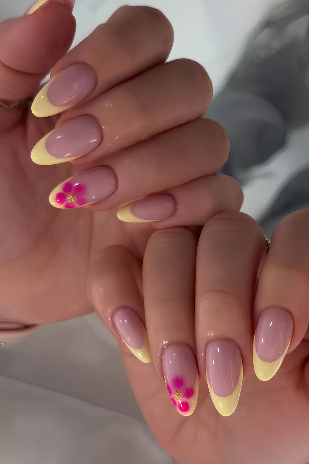 Almond-shaped nails with yellow French tips and pink floral designs on two accent nails, one with a small gold bead.