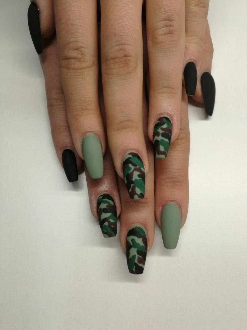Hand with coffin-shaped nails, some painted solid military green, others with a camouflage pattern.