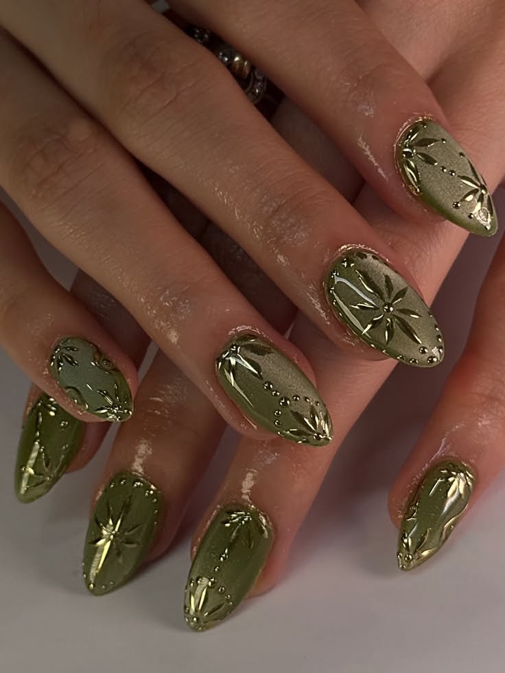 Close-up of a person's hands with military green almond-shaped nails featuring raised metallic designs.