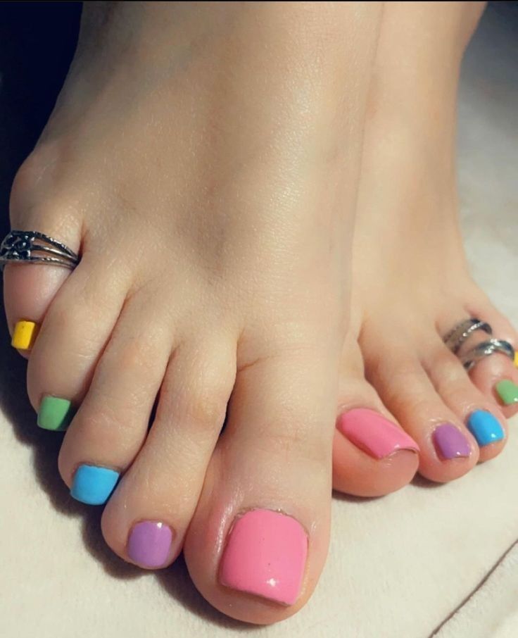 Close-up of a person's feet with each toenail painted a different pastel color, including pink, purple, blue, green, and…