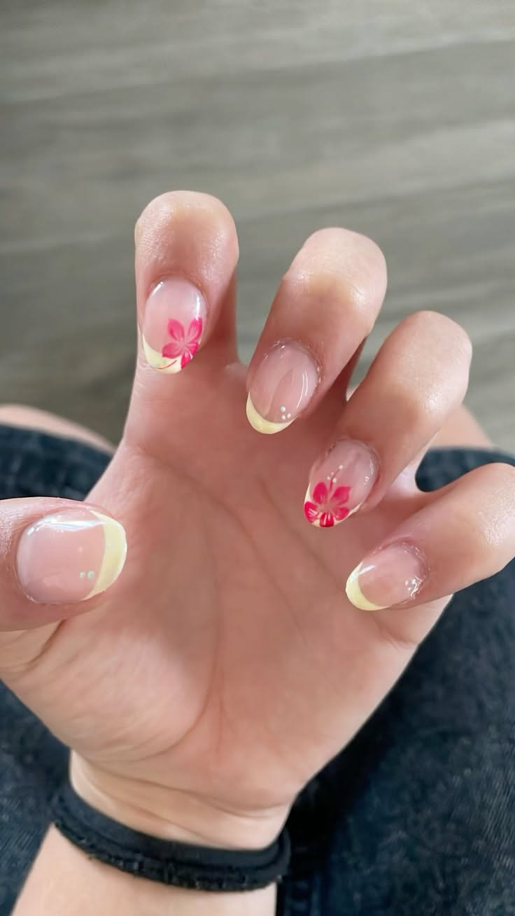 Close-up of a person's hand with short, clear-coated nails featuring yellow French tips and small pink flower decals.