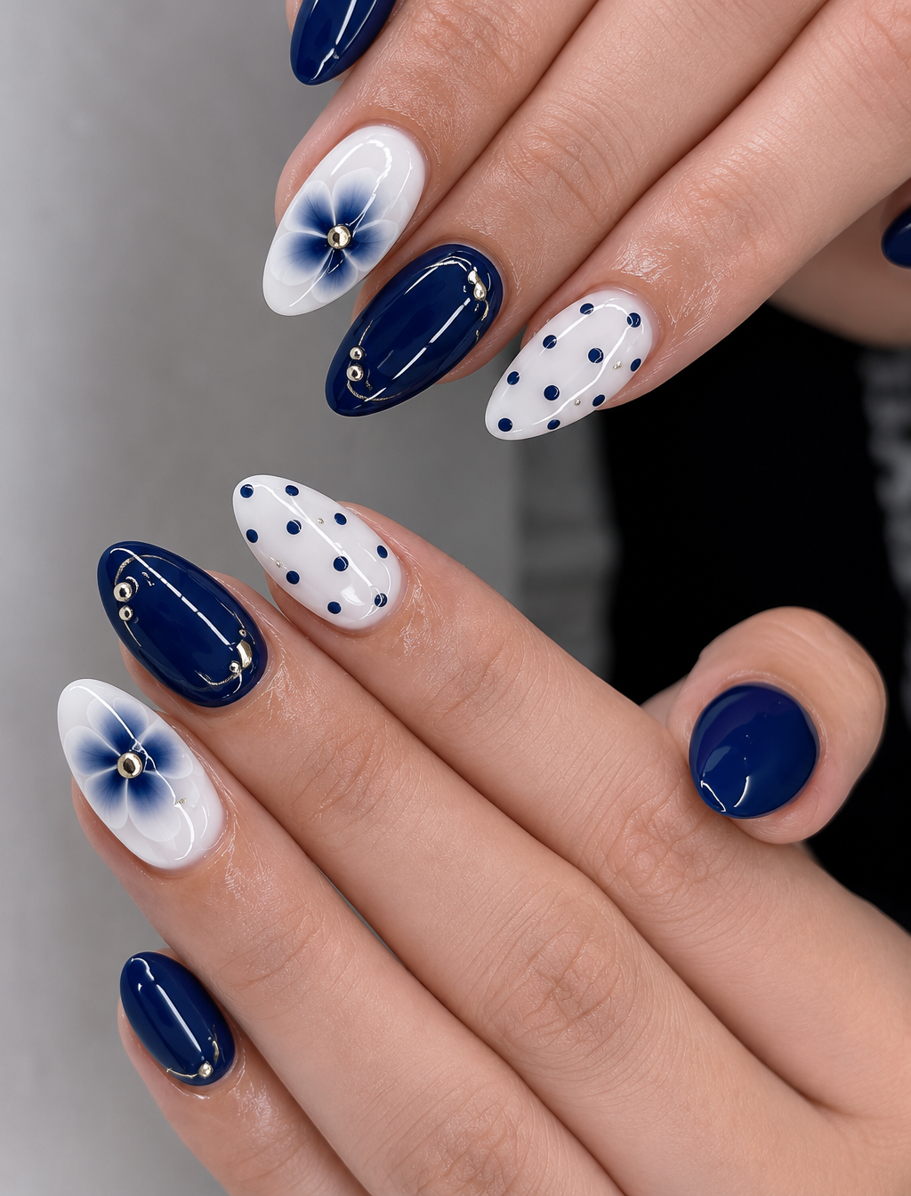 Close up of manicured hands with almond nails featuring navy blue and white polish, polka dots, and floral designs.