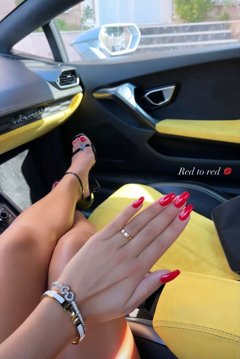Person in a car with red coffin-shaped fingernails and red painted toenails wearing black heels.