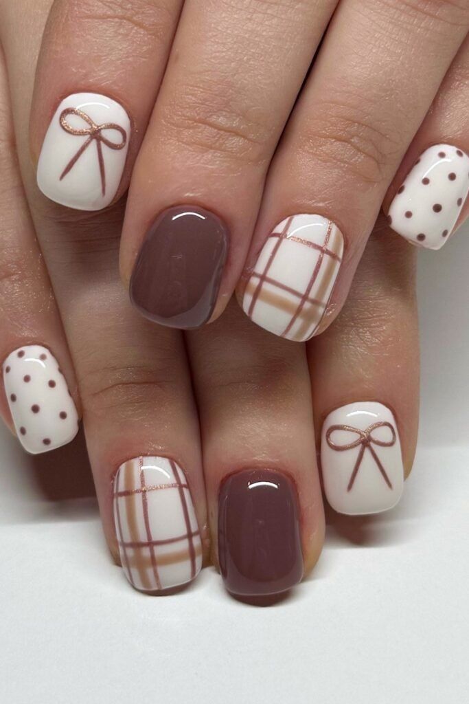 Close up of five fingernails with various fall-themed designs. Some are solid brown, some have white with brown polka dots…