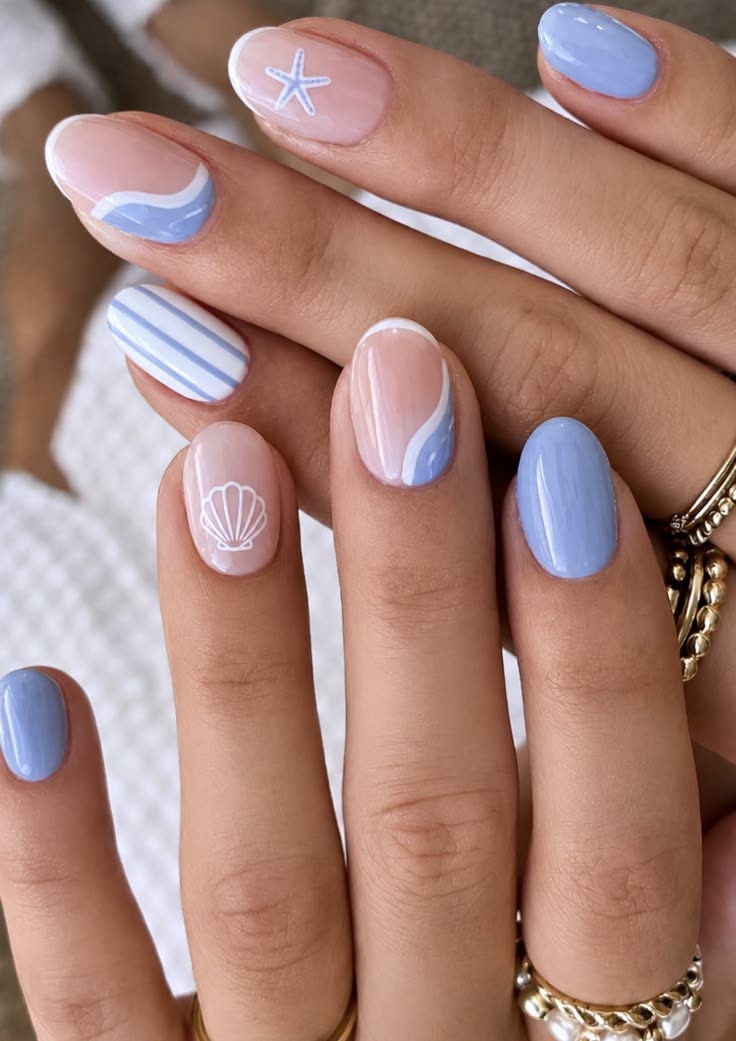 Close up of hands with short, rounded nails painted with a variety of light blue and neutral beach-themed designs.
