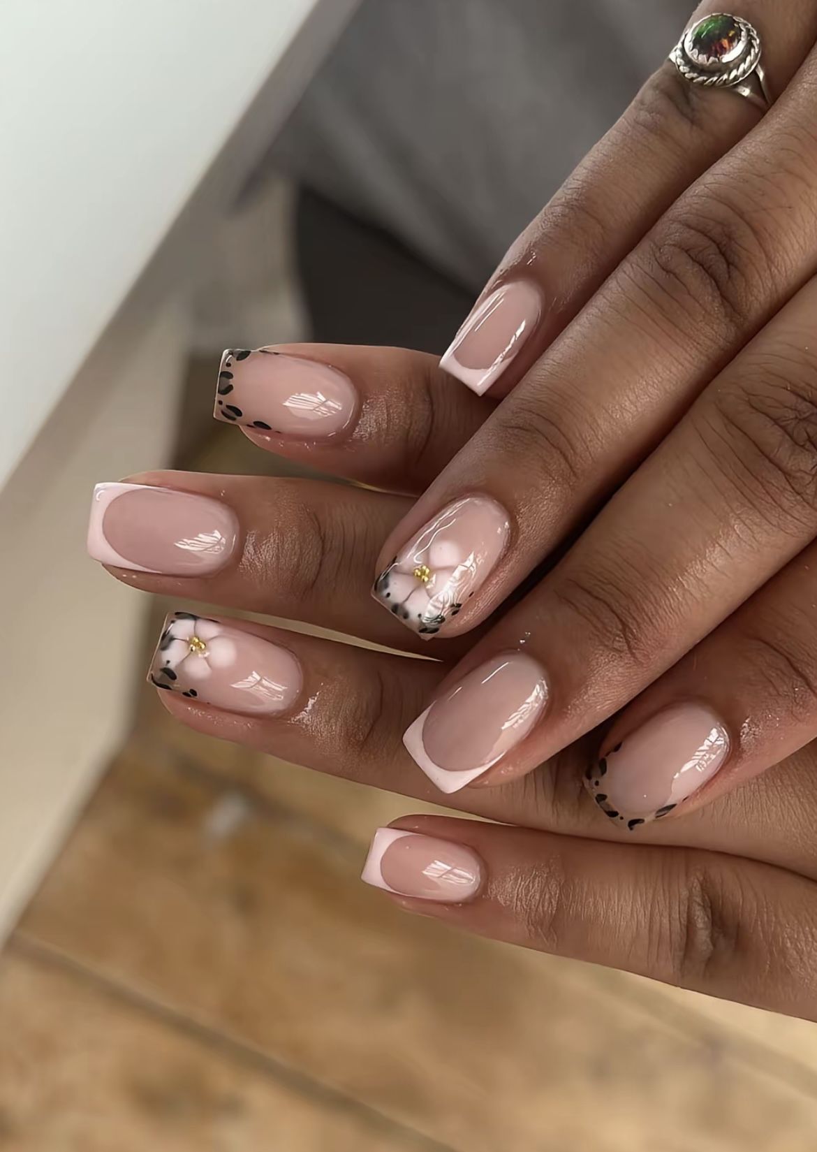 Close-up of a person's hands with short, squared nails. Some nails have white tips, others have a leopard print, and some…