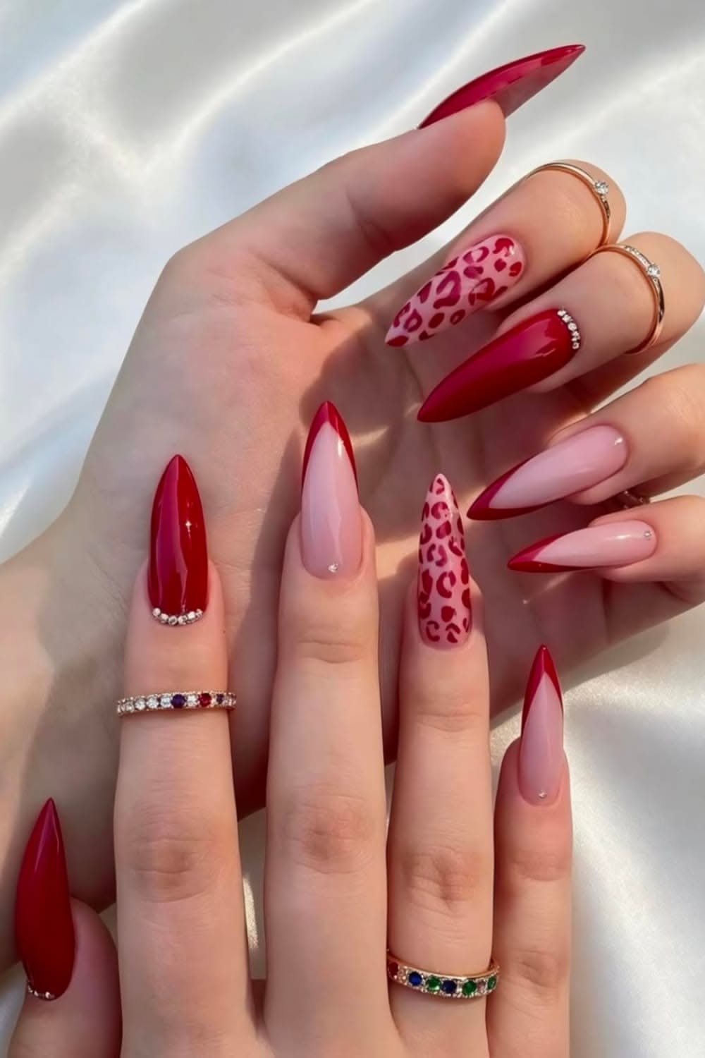 Hand with long, pointed stiletto nails. Some nails are solid red, others have red French tips or red leopard print.