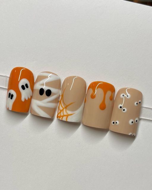 Five artificial nails displayed in a row, each with a different Halloween-themed design like ghosts, mummies, spiderwebs…