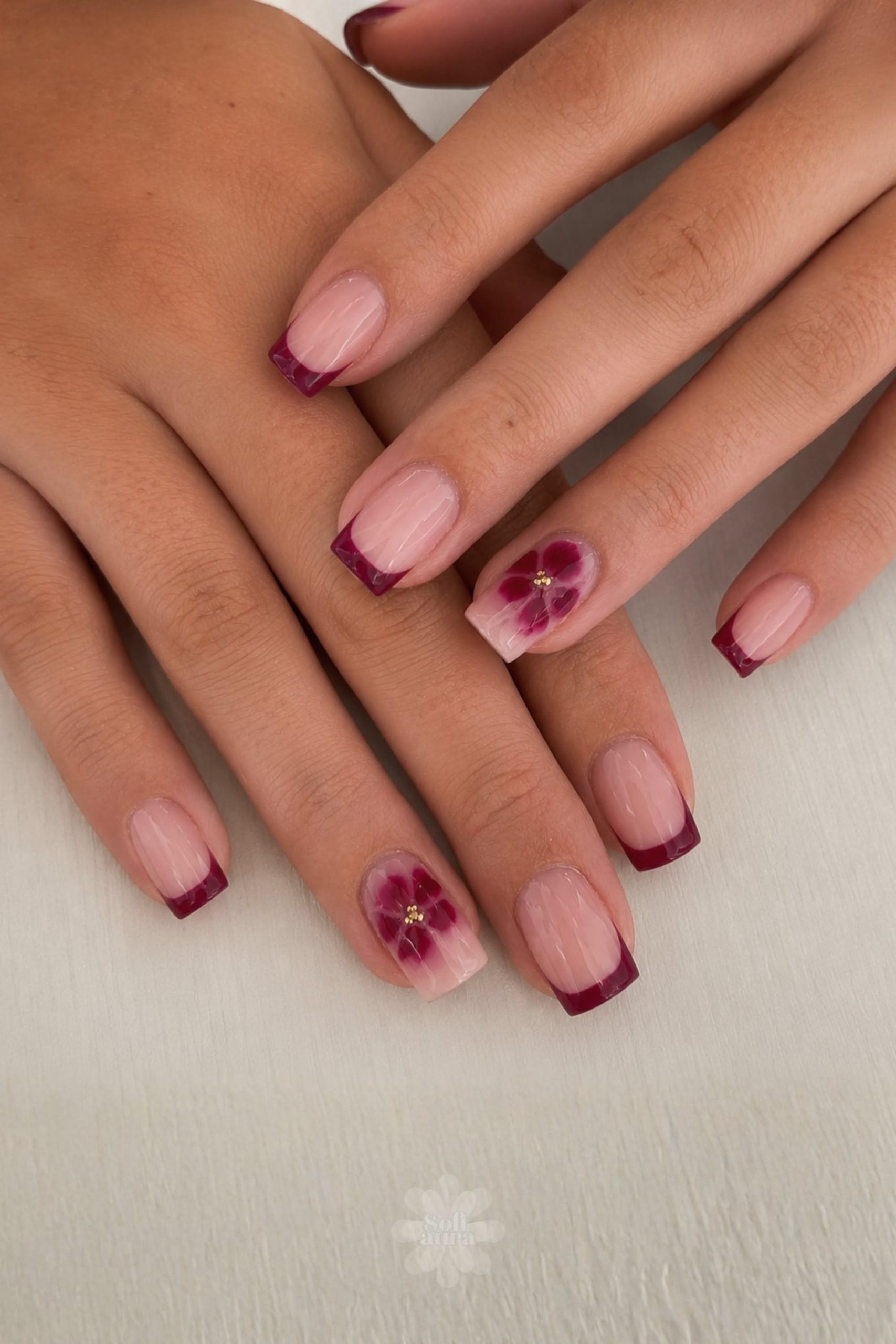 Close-up of hands with short nails featuring French tips with dark red polish and one accent nail with a red flower design.