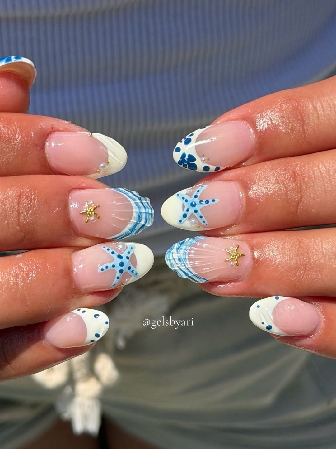 Close-up of manicured fingernails featuring ocean-inspired designs like blue starfish, seashells, and white and blue…