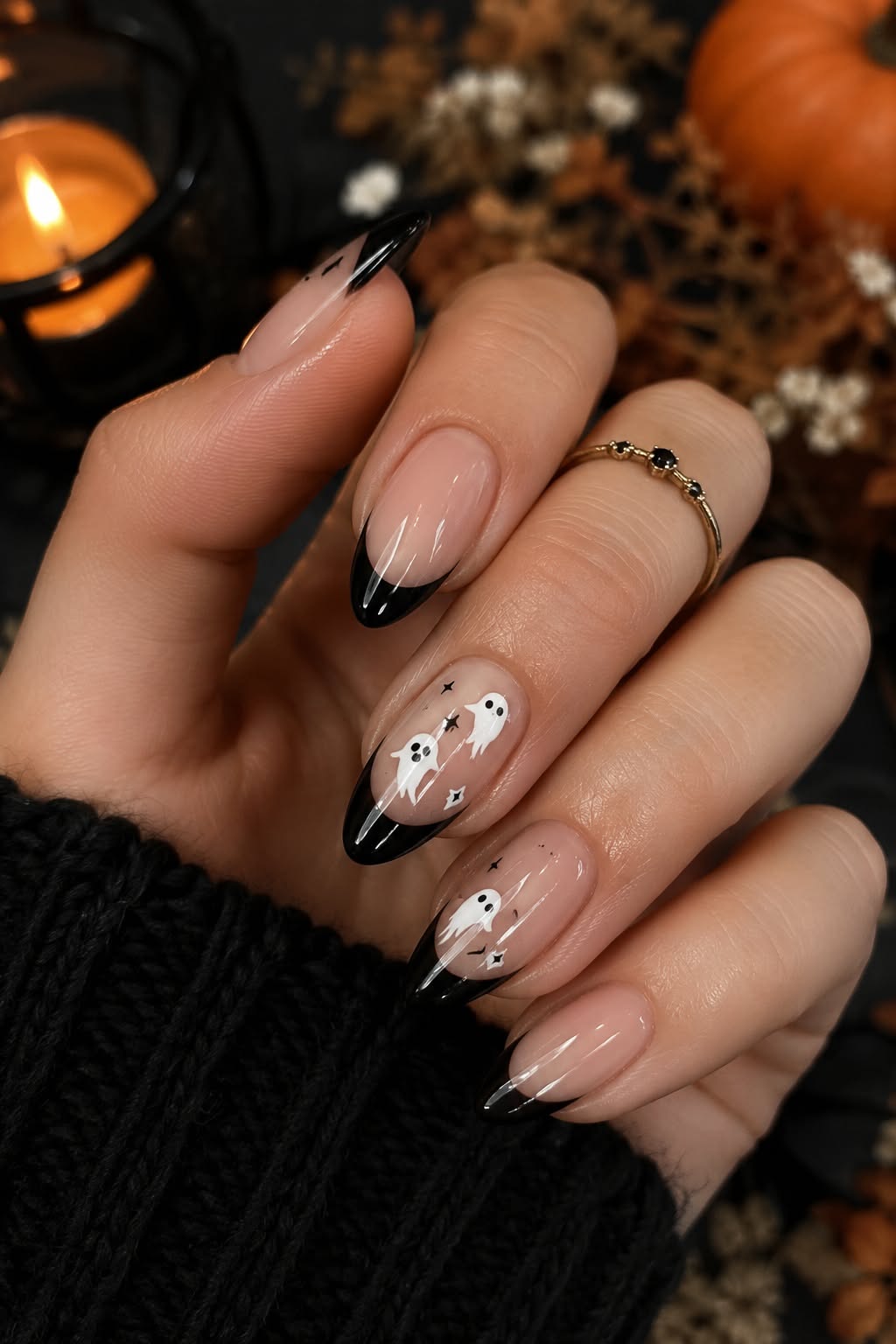A hand with an almond-shaped manicure featuring black French tips and whimsical white ghost designs with stars and bats.