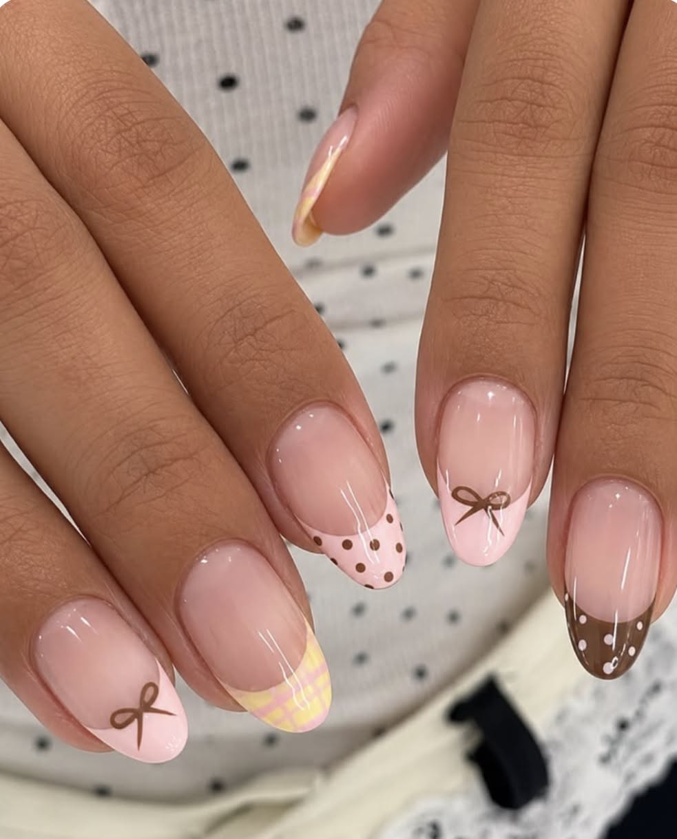 Close up of manicured hands with various French tip designs including plaid, polka dots, and small bows on rounded nails.