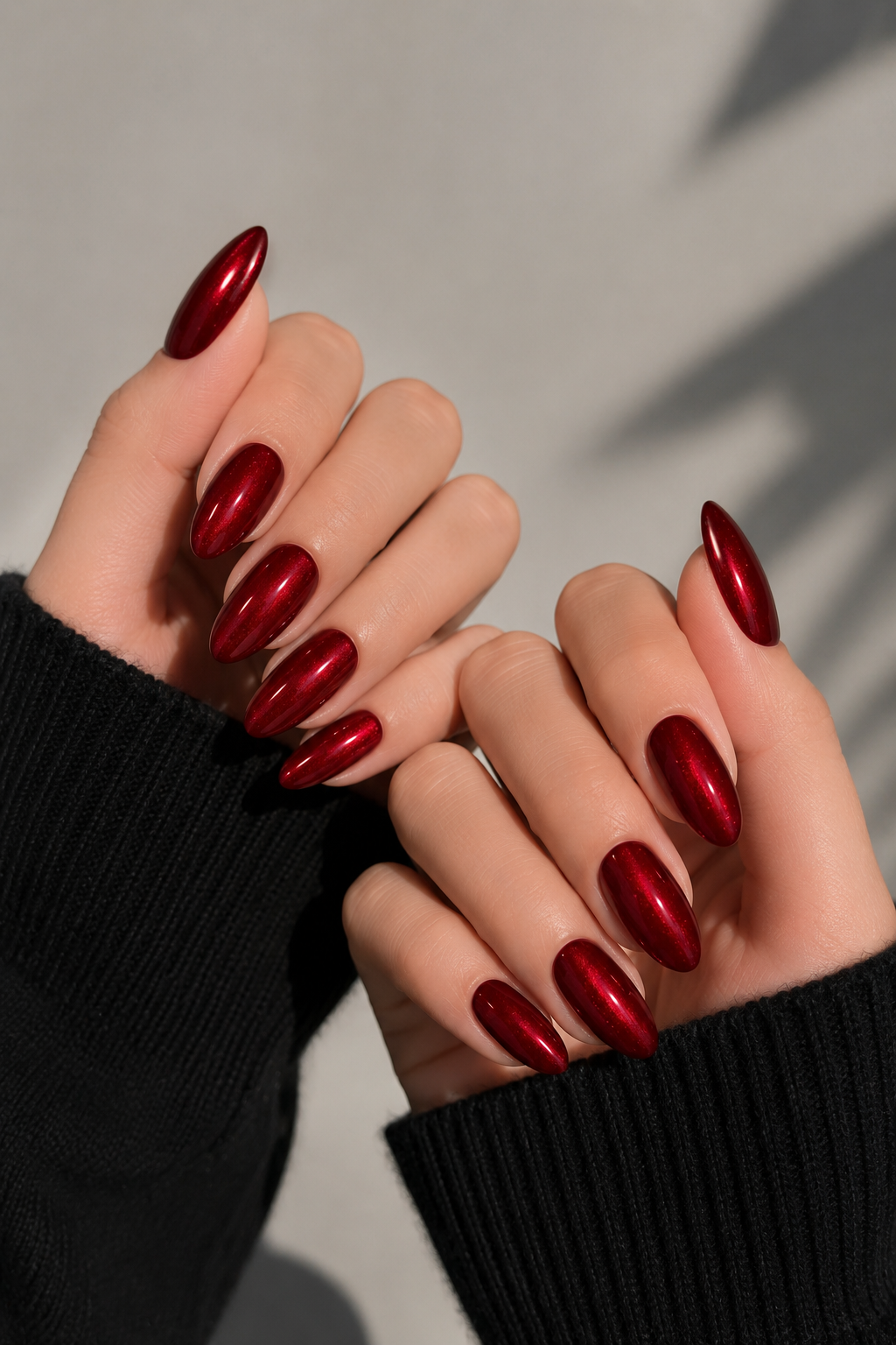 Hands with long, glossy, metallic red almond-shaped nails, partially visible black sweater sleeve