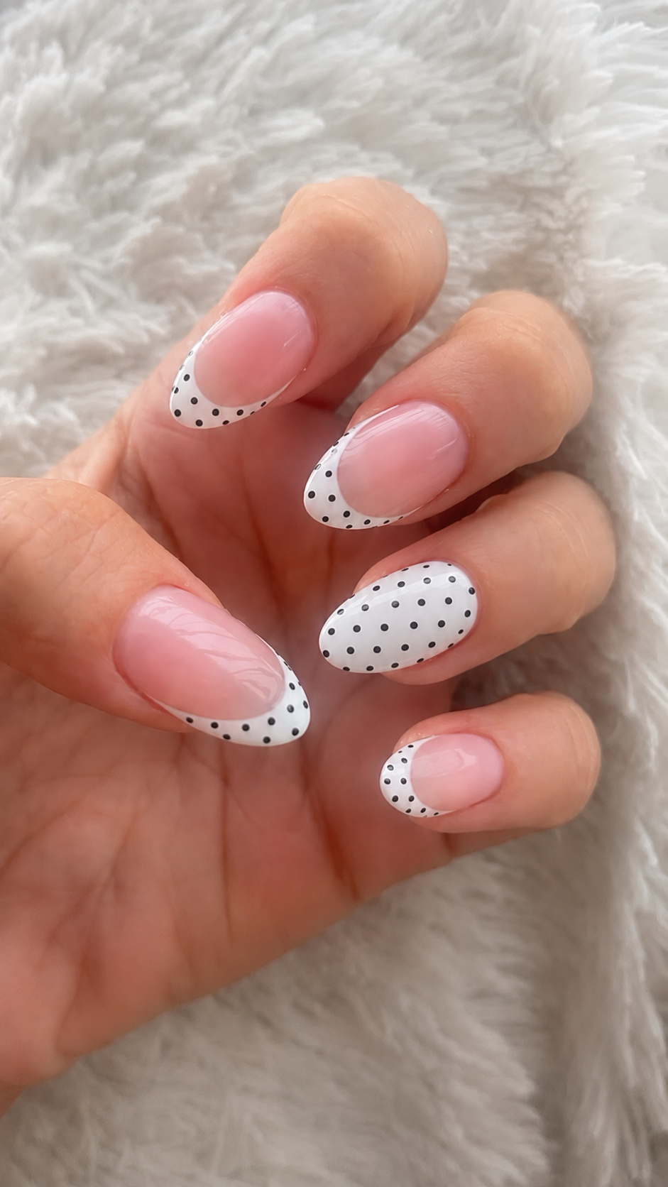 A hand with neatly manicured nails featuring a clear base with white polka dot french tips.