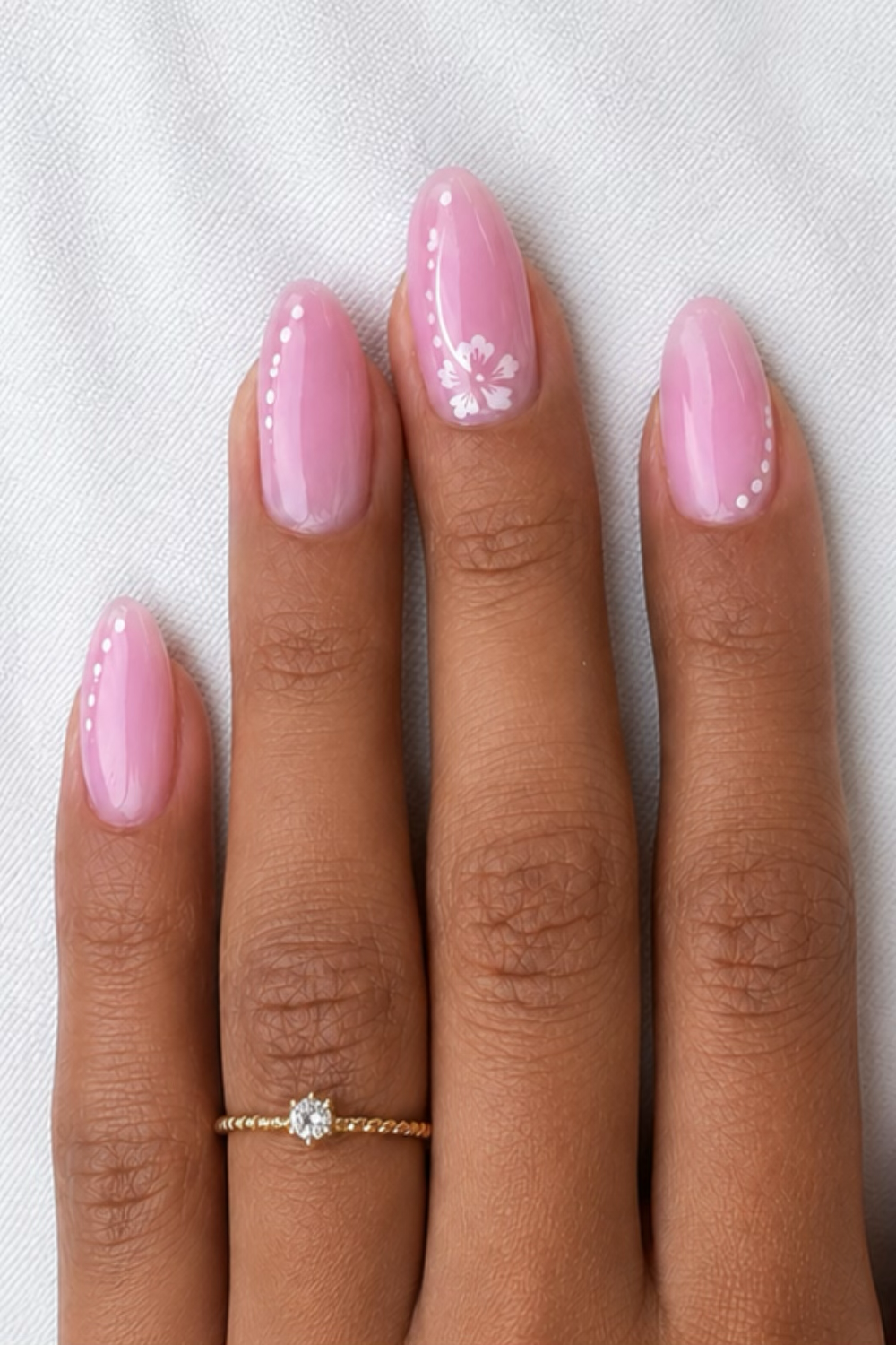 Close-up of a hand with pink nails, one nail features a small white blossom design, others have delicate white dots.