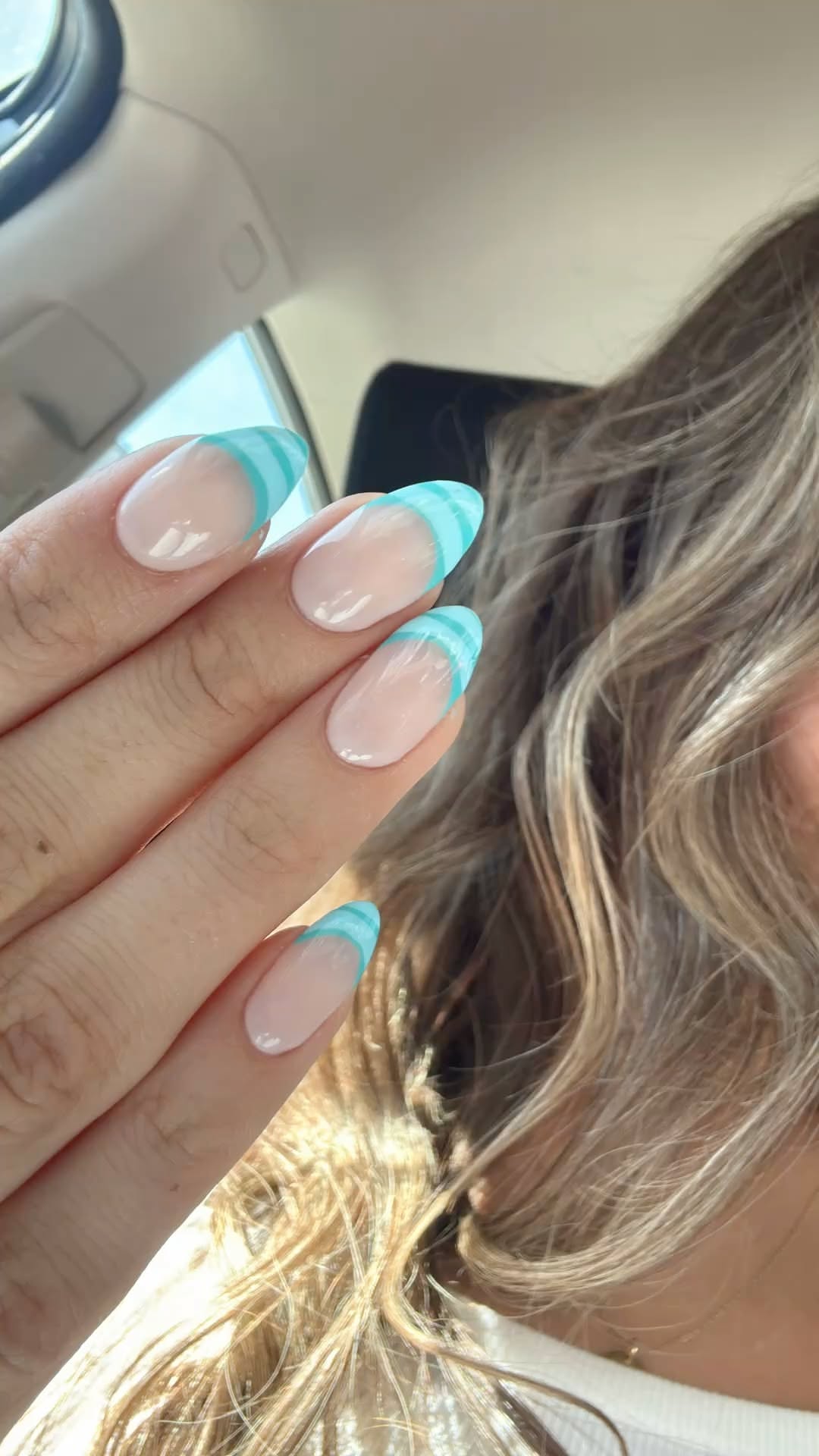 Close-up of a person's hand with light pink nails featuring blue and white striped tips.