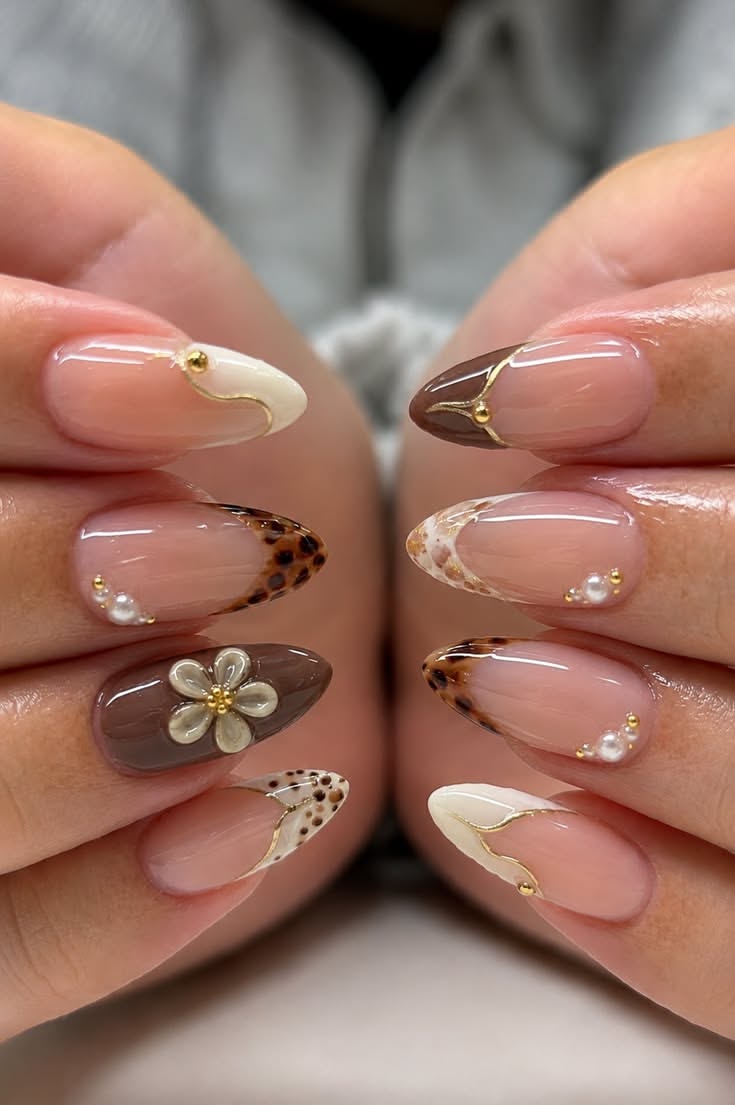 Almond-shaped nails in warm brown and cream with gold lines, pearl accents, and animal print details.