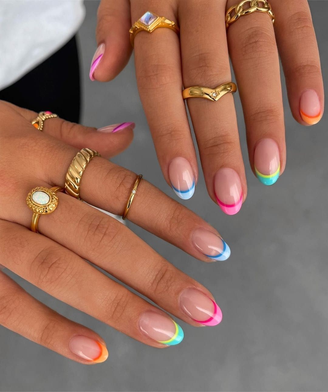 Close-up of hands with short nails featuring a rainbow French manicure with different color tips.