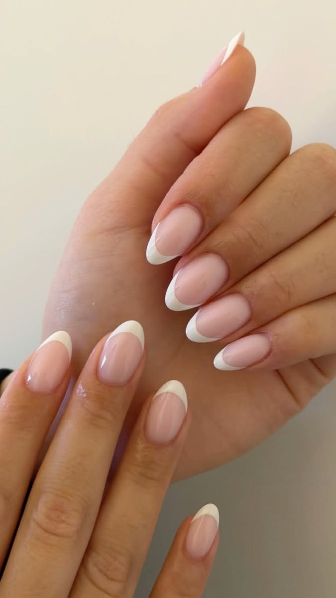 Close up of a person's hands with almond-shaped nails, each adorned with a white French tip.