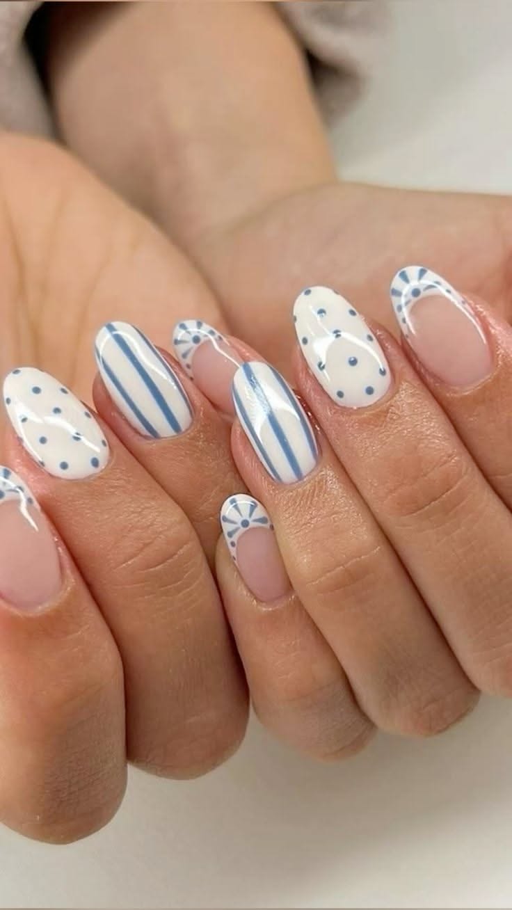 Close-up of a person's hands with manicured nails. The nails feature white polish with blue polka dots, blue vertical…