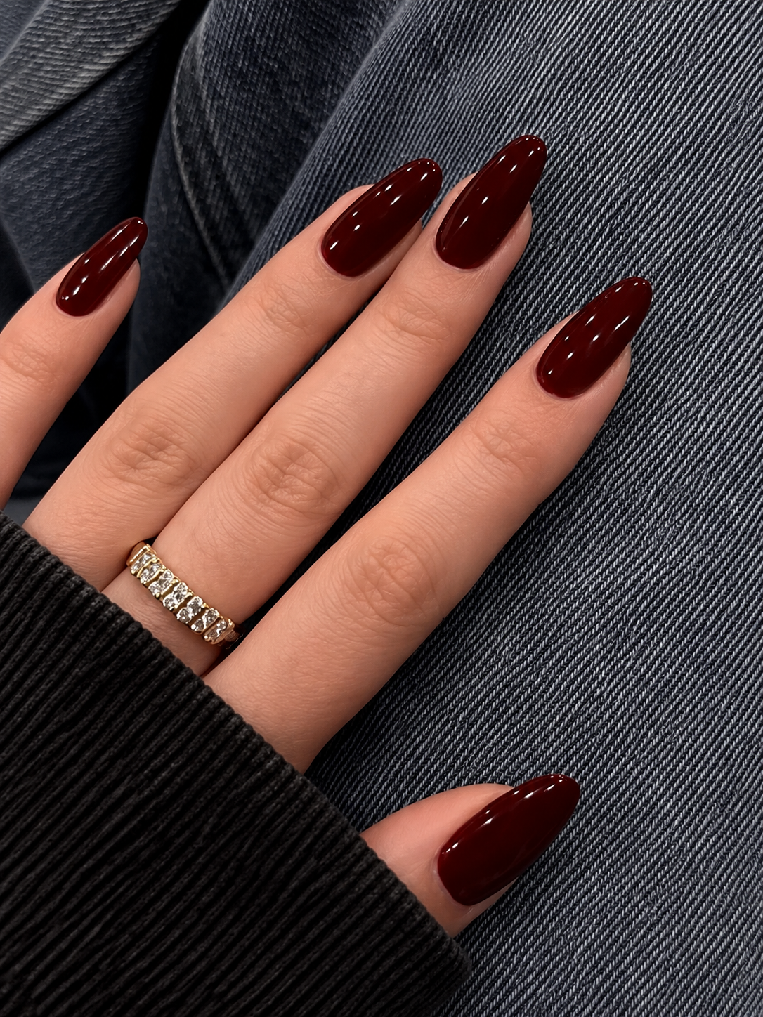A hand with glossy, deep red almond-shaped nails rests against dark denim fabric.