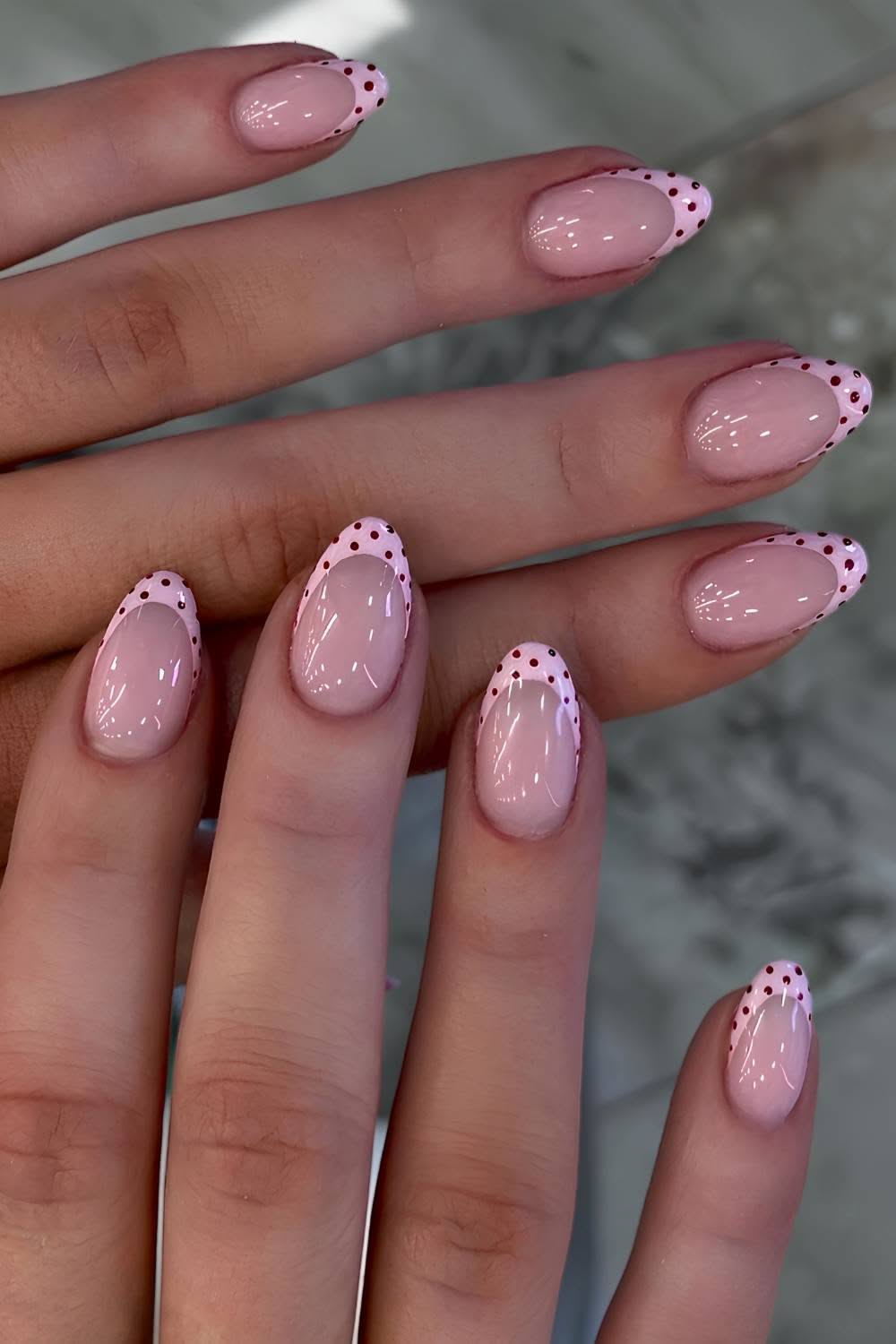Light pink nails with white tips featuring small red polka dots along the edge