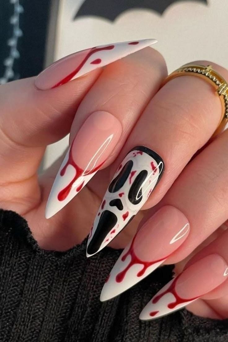 Long, pointed nails with a French tip style, featuring red blood drip designs and one nail with a Ghostface mask.