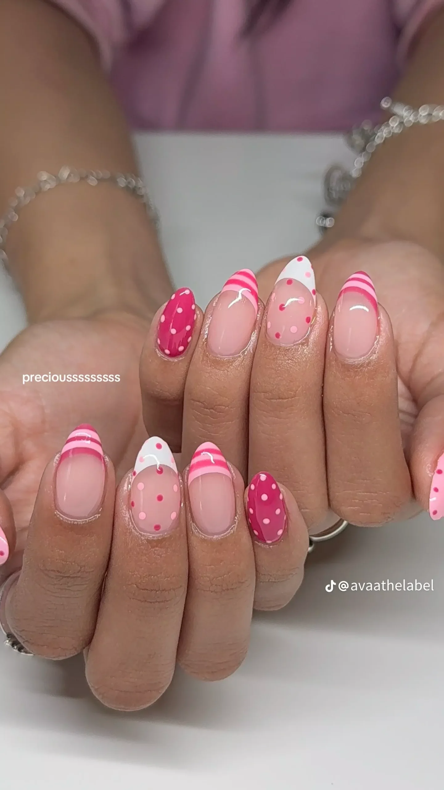 Close-up of pink almond-shaped nails with alternating polka dots and stripes, some with French tips.