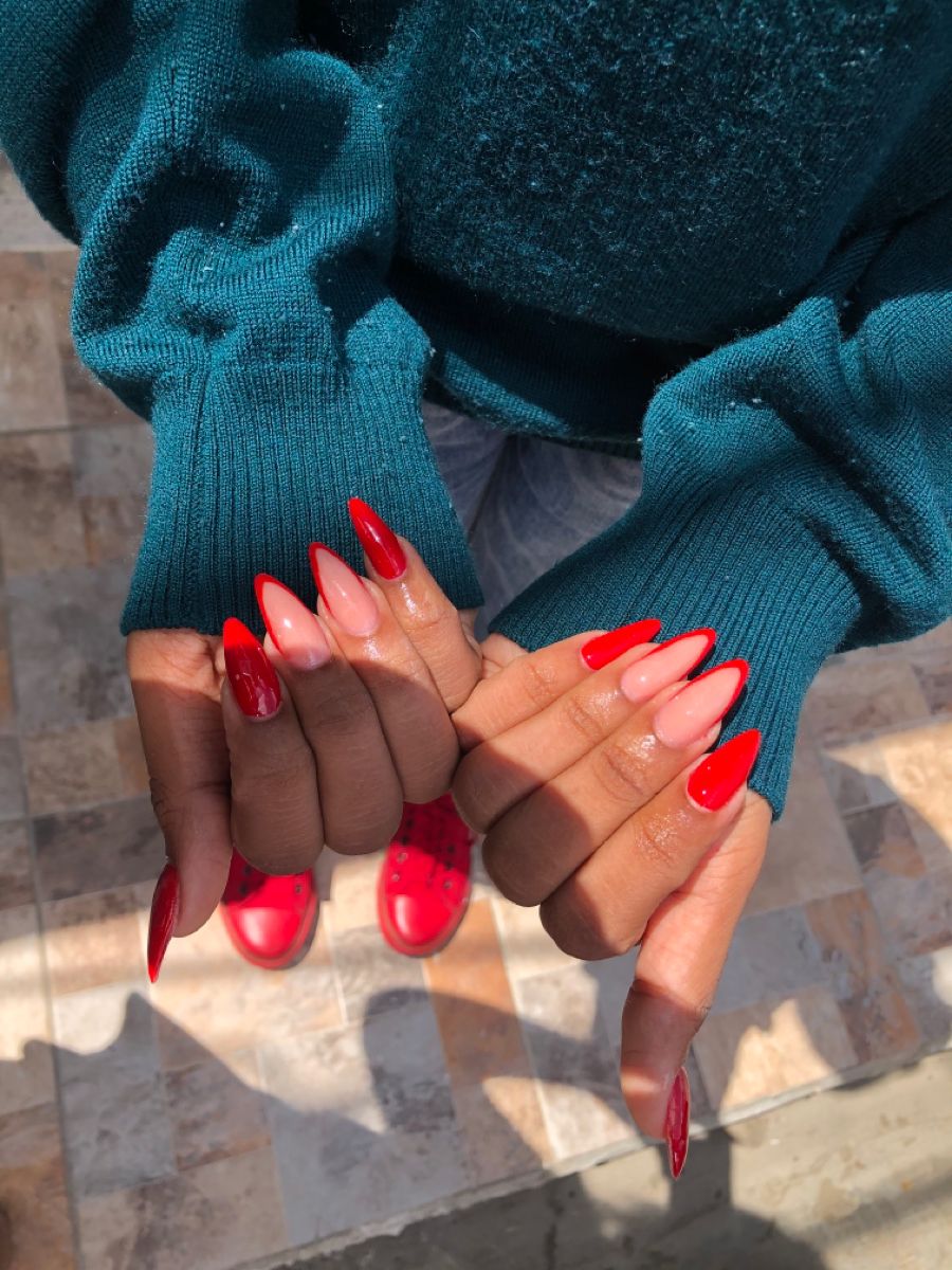 Overhead view of hands with long, pointed nails featuring a red French tip design, wearing a teal sweater.