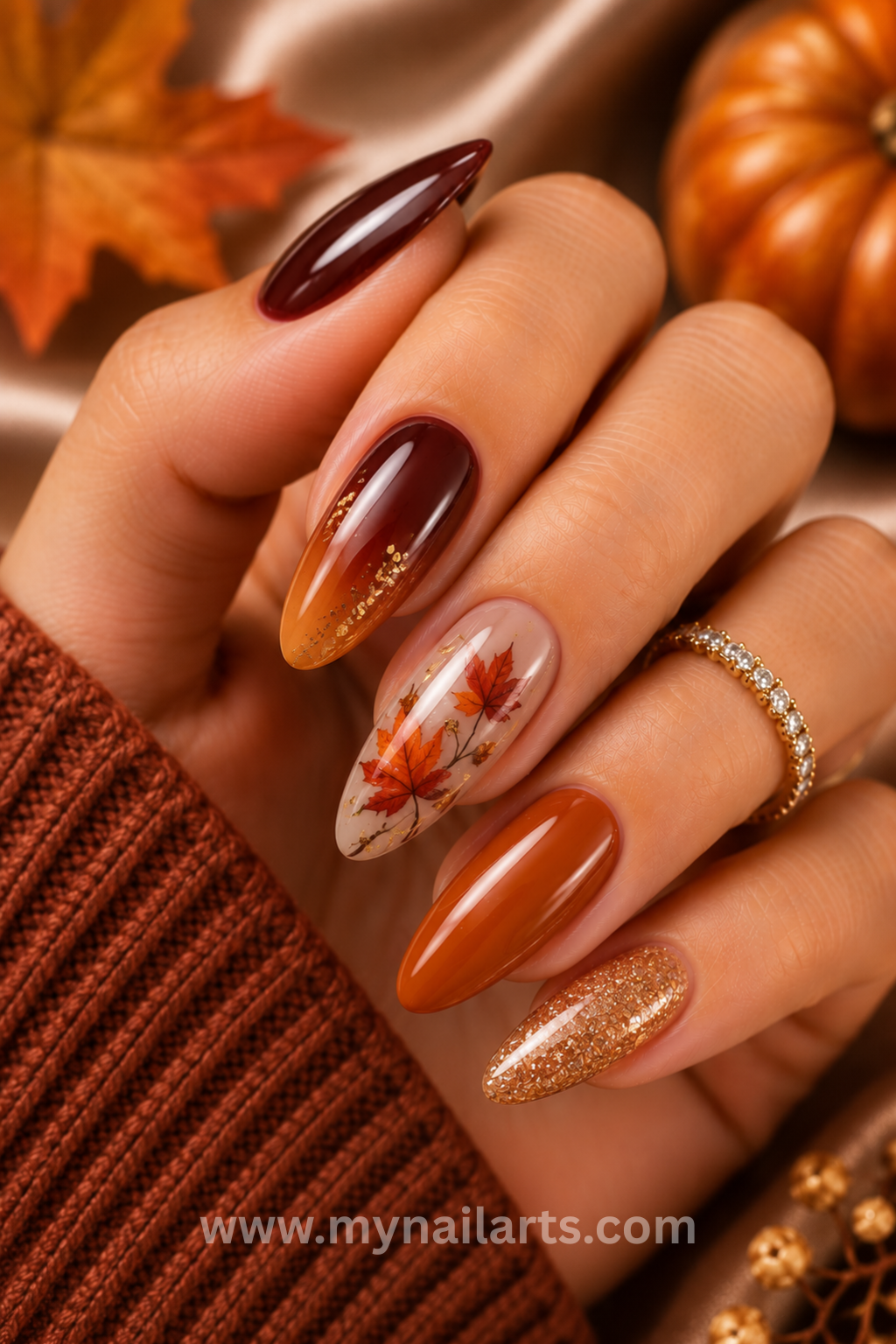 Close up of a hand with various autumn-themed nail designs, including deep red, orange, glitter, and a leaf pattern.