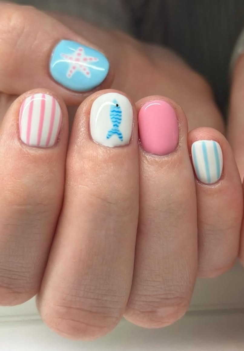 Close-up of a hand with short nails painted with beach-themed designs including a starfish, fish, and stripes.