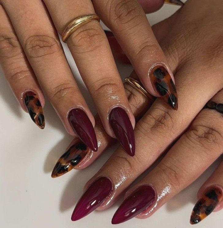 Close up of hands with almond-shaped nails, some painted solid deep red, others with a tortoiseshell pattern.