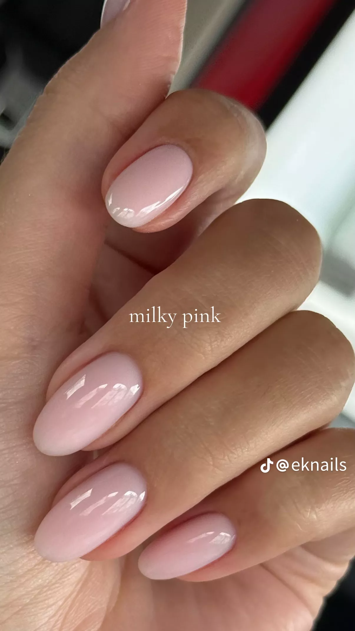 Close-up of a hand with oval-shaped nails painted in a sheer, milky pink polish.