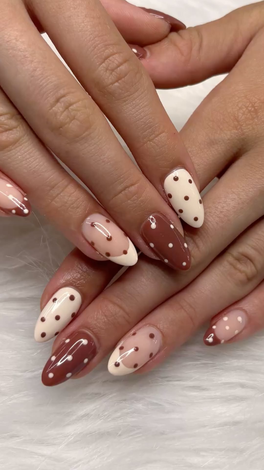 Close-up of hands with almond-shaped nails, featuring a brown and cream polka dot design.