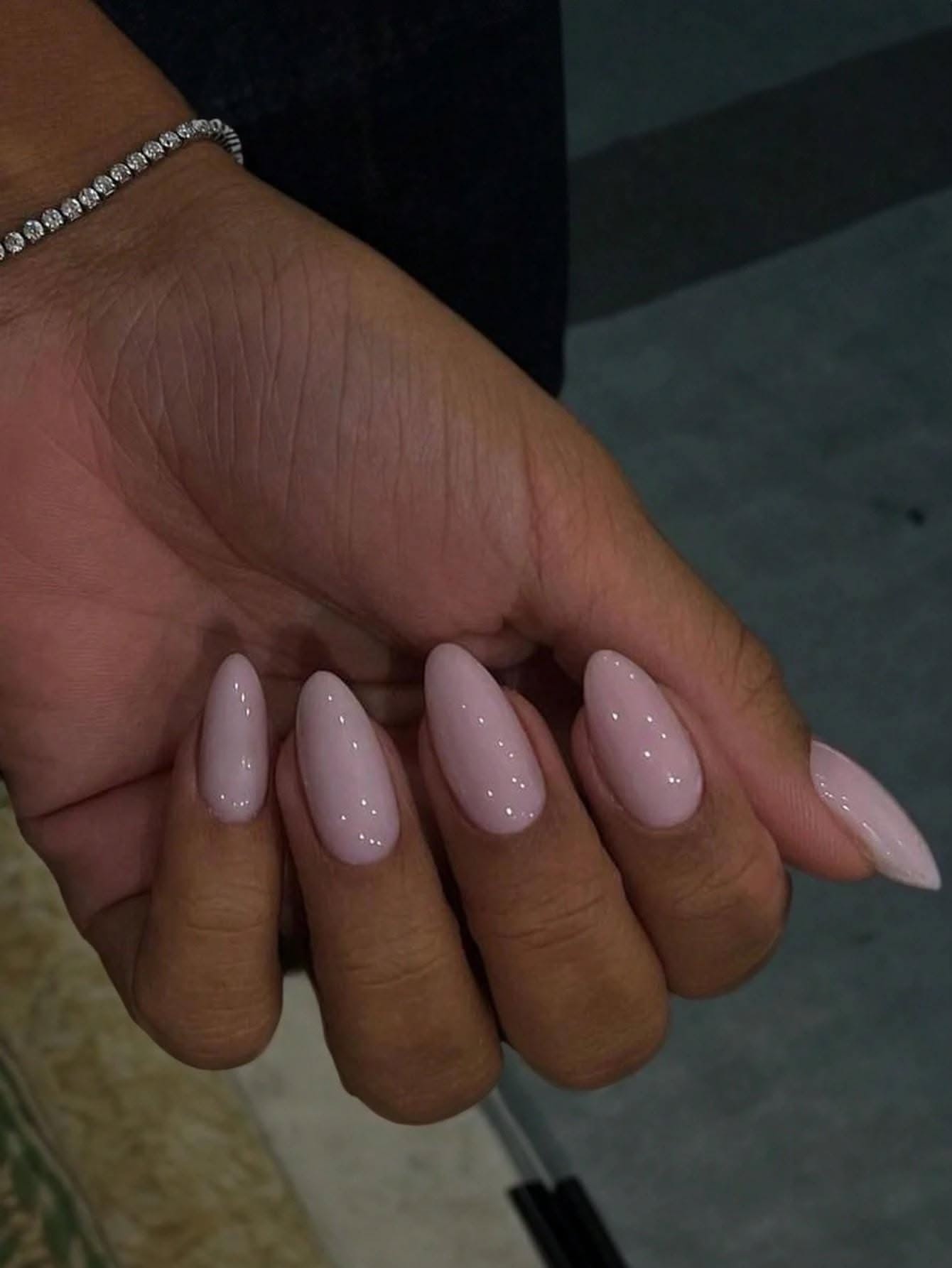 Close-up of a hand with milky pink, glossy, almond-shaped press-on nails.
