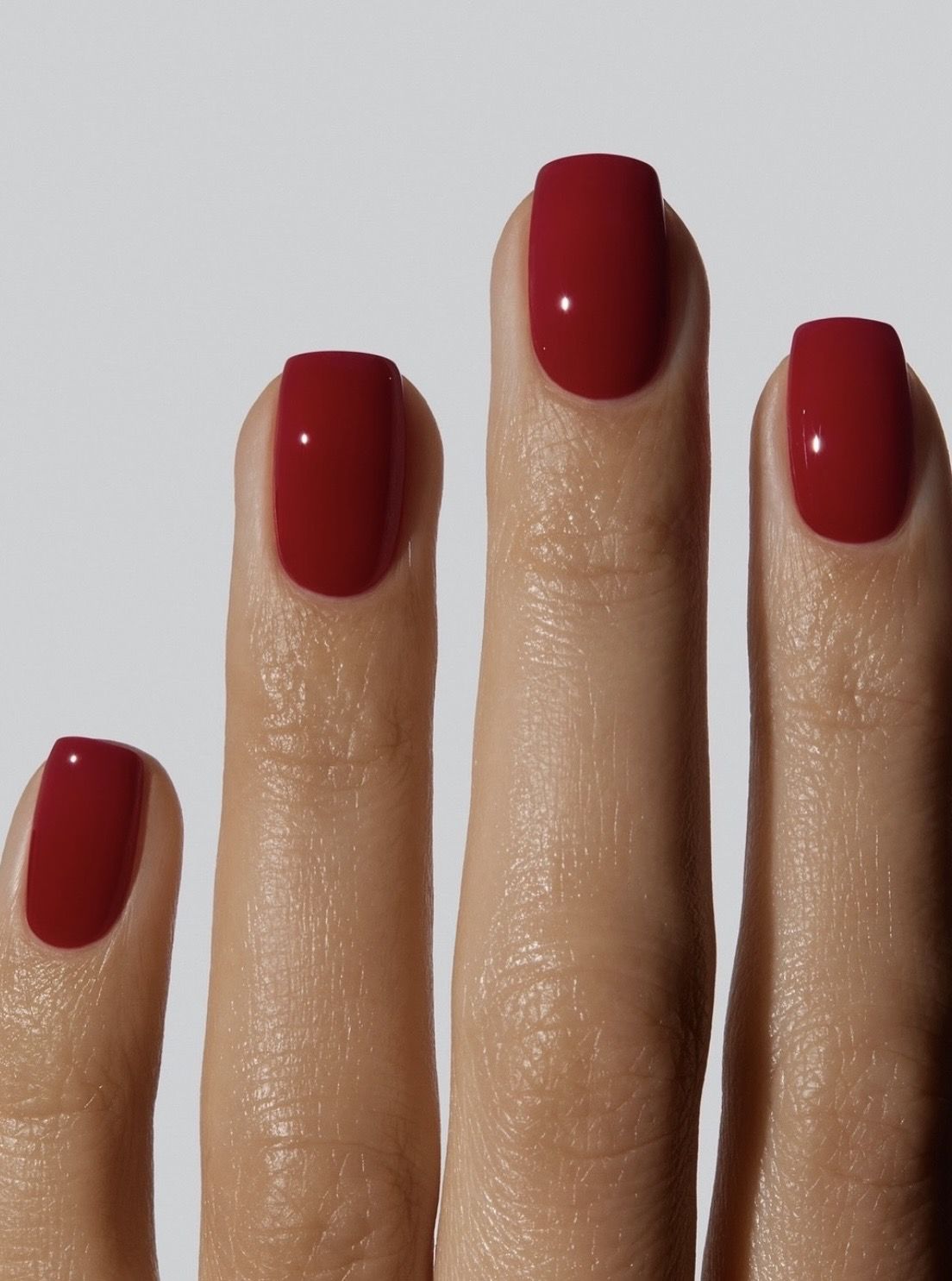 Four fingers with perfectly manicured, glossy cherry red nail polish.