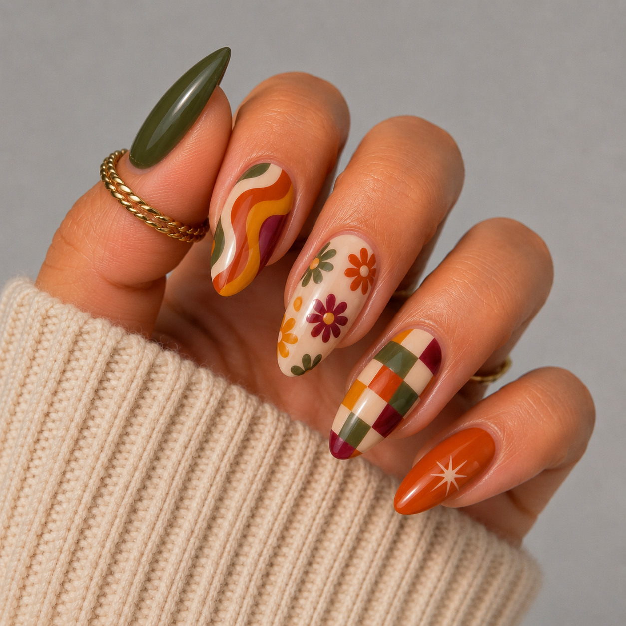 Hand with five almond-shaped nails, each painted with a distinct fall-themed retro design.