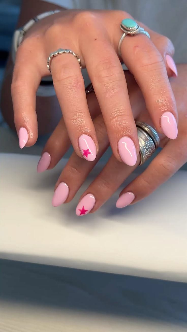 Hands with short, light pink oval nails. Two nails feature a bright pink star design.