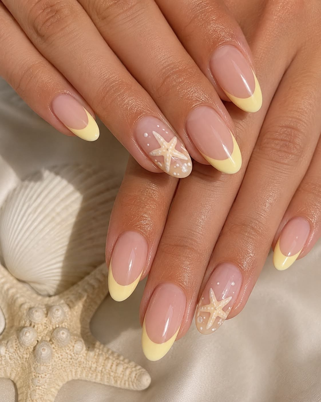 Manicured hands with yellow French tips and a starfish design on one accent nail.