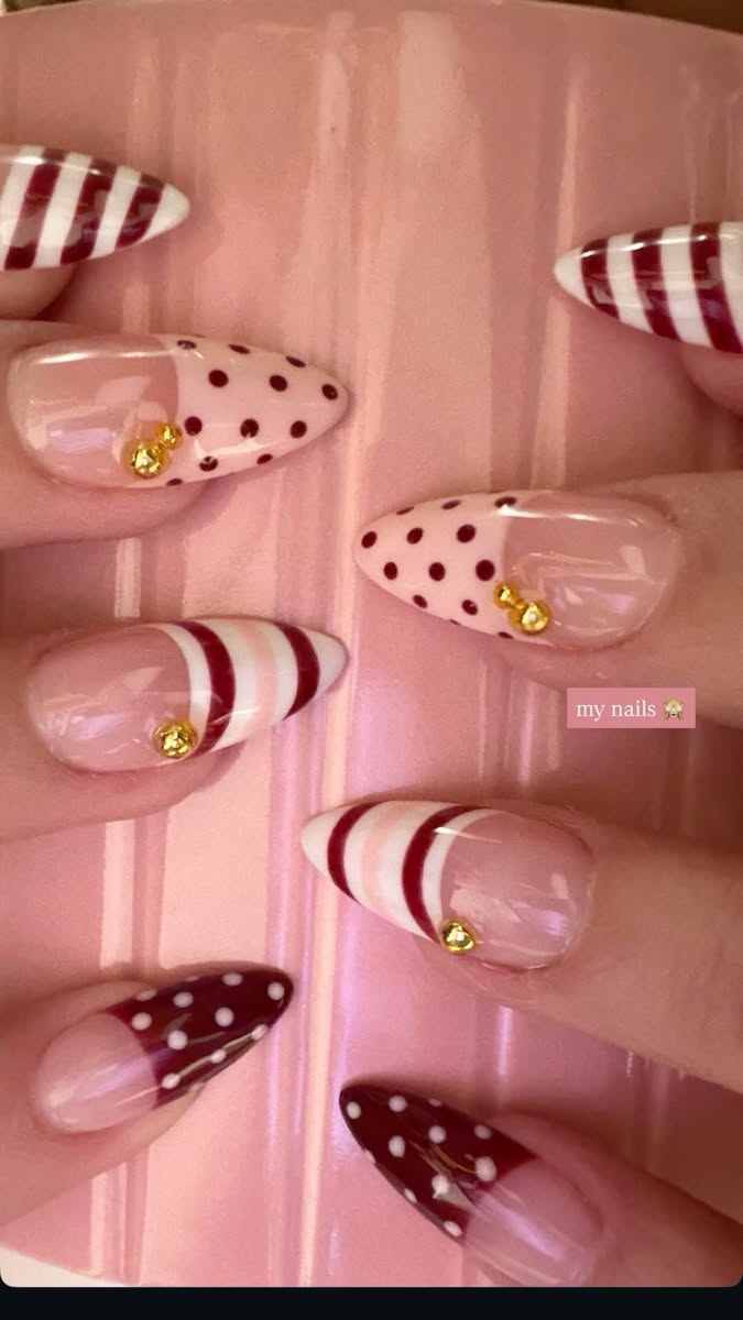 Close-up of several pointed nails, some with red and white stripes, others with red polka dots on a light pink base, and…