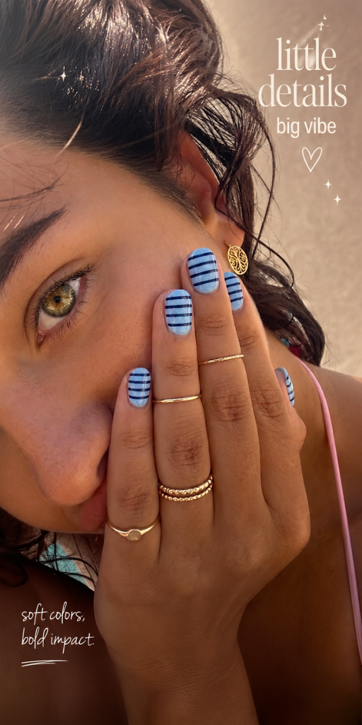 Close-up of a person's face and hand with light blue nails that have thin navy horizontal stripes.