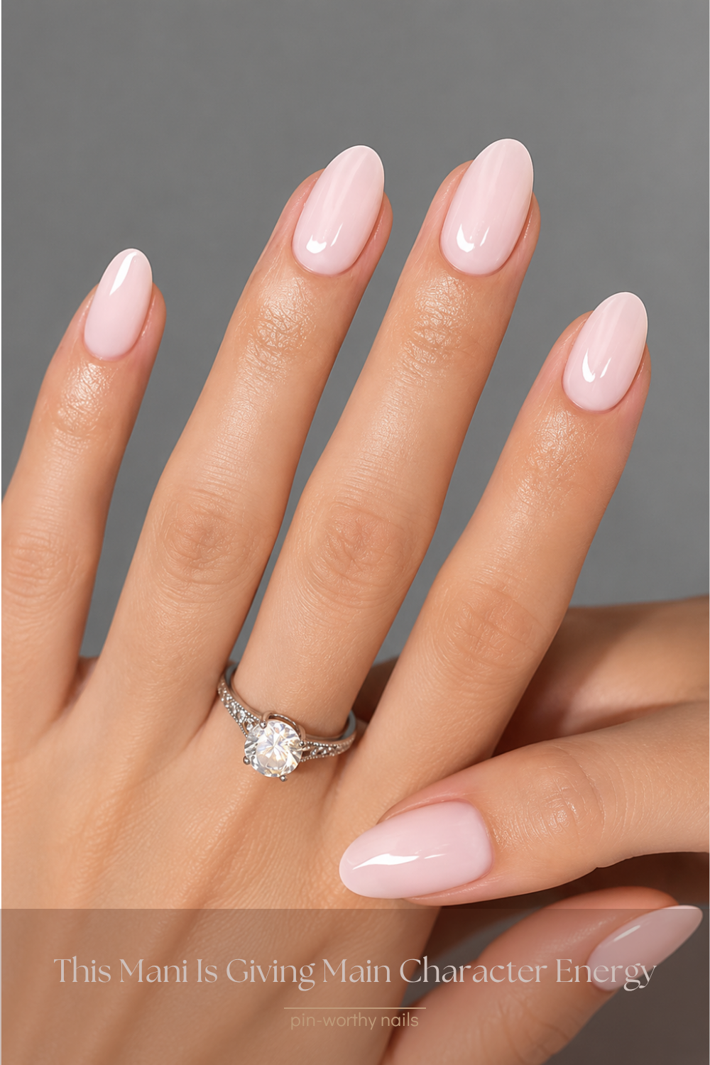 Hand with light pink oval nails and a solitaire diamond ring on the ring finger.