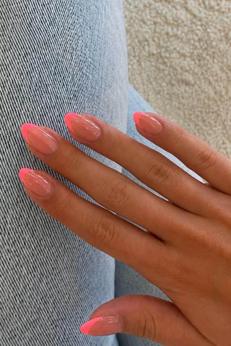 Hand with five fingers displaying almond-shaped nails with a clear base and bright neon pink French tips.